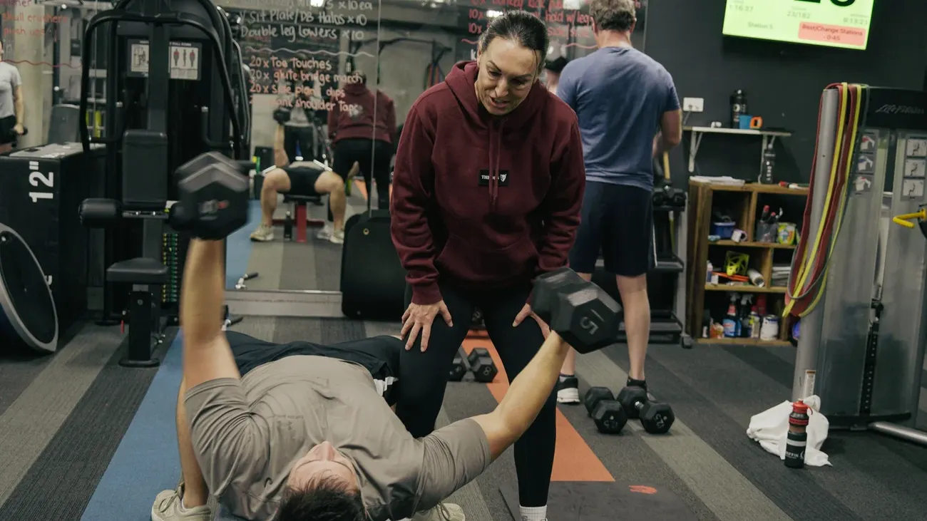 Nicole spotting a member through a dumbbell press while others train around them